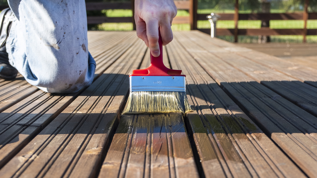 Copy space. Painter paints the surface of a wooden board with a brush. Protection of wooden materials from rotting and water. Summer day and sun rays.